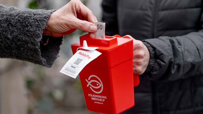 En person kaster penge i en rød samlerekasse.
