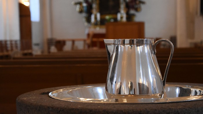 En sølv kaffe-kanne står på bord i kirke.