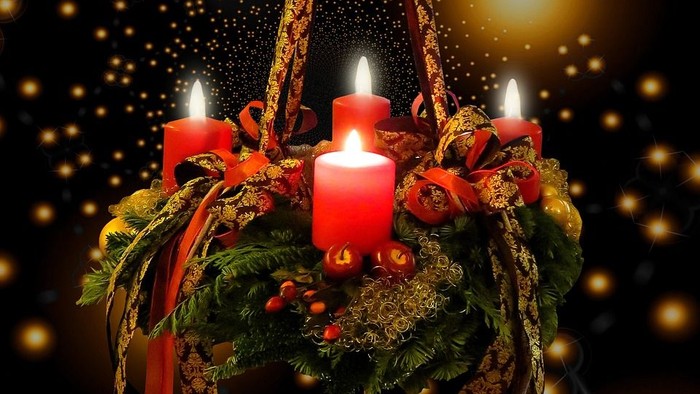 Ein Adventskranz mit vier brennenden Kerzen vor einem funkelnden Hintergrund