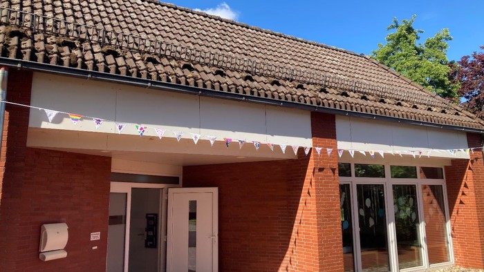 Ein rotes Ziegelgebäude mit weißer Tür und Fensterläden unter einem Ziegeldach