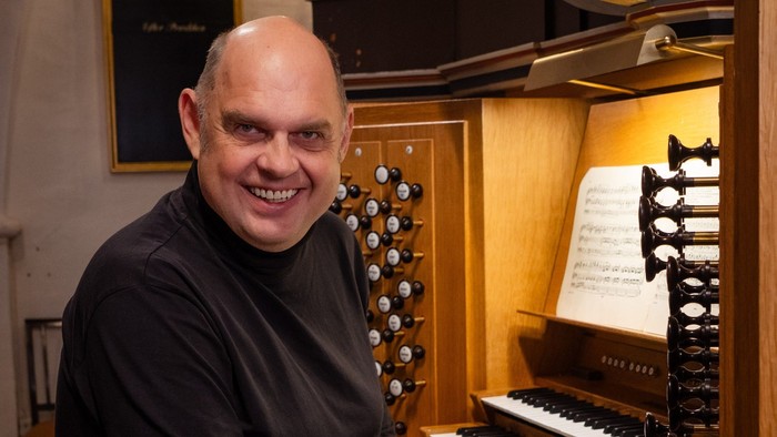 Mand sitter ved et orgel og smiler til kameraet