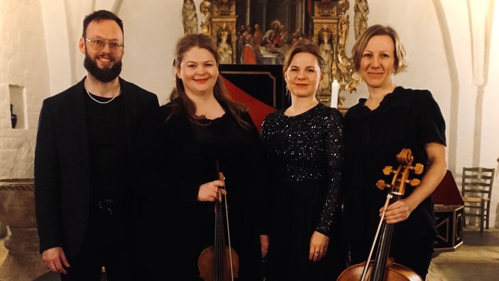 Et kvartet musikere med strygeinstrumenter, der poserer sammen indendørs i formelt tøj.