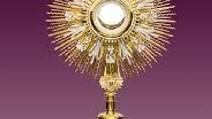 Goldene Monstranz mit Kreuz und Strahlenkranz auf lila Hintergrund