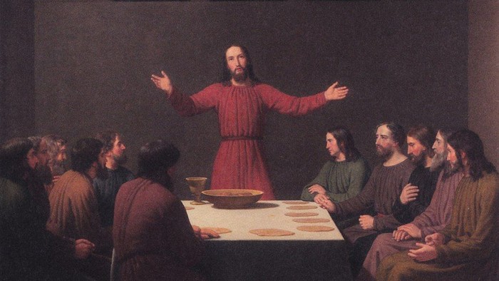 En gruppe mennesker sidder om en bord, mens en mand i rød kappe taler.