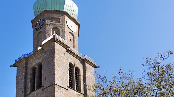 Hohe Kirche mit grünem Turm und Kreuz, umgeben von Bäumen und Menschen