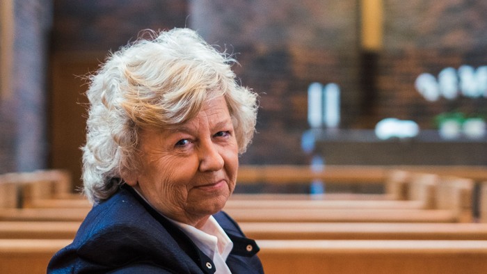 En kvinde sidder i en kirkebænk og smiler.