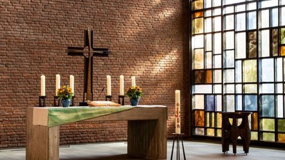 Ein Kirchenaltar vor einem Ziegelsteinwall und buntem Glasfenster