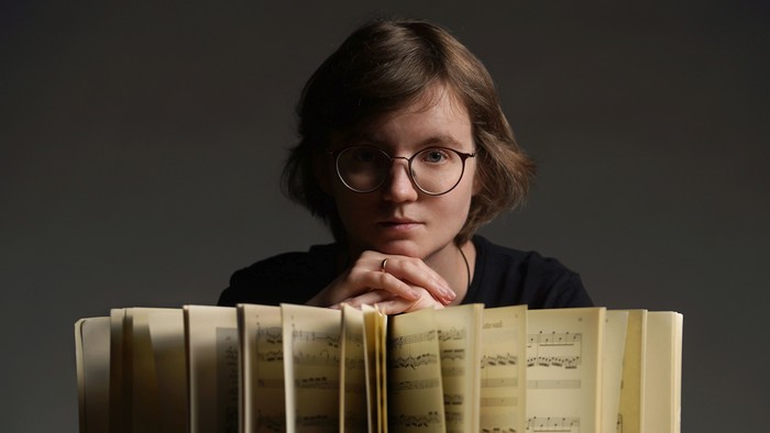 Eine Frau mit Brille lehnt an einem Stapel Bücher.
