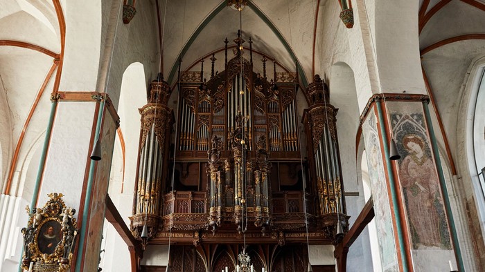 Historische große Pfeifenorgel in einem prunkvollen, gewölbten Kircheninnenraum mit hölzernen Kirchenbänken und dekorativen Wandmalereien.
