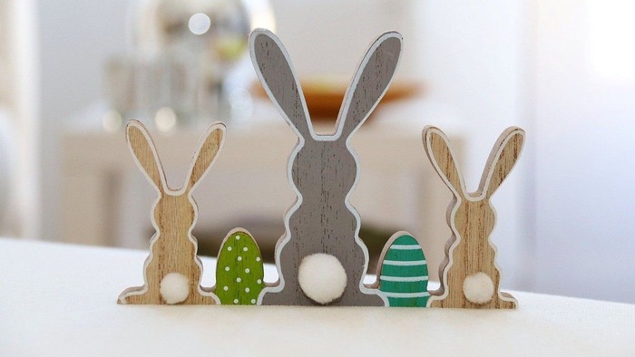 Drei Holzbunny mit Ostereiern auf weißer Oberfläche