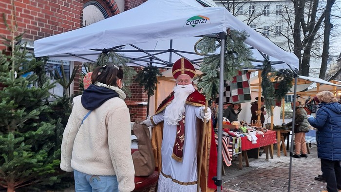 Ein Mann im Weihnachtsmannkostüm steht unter einem weißen Zelt und spricht mit einem anderen Mann.