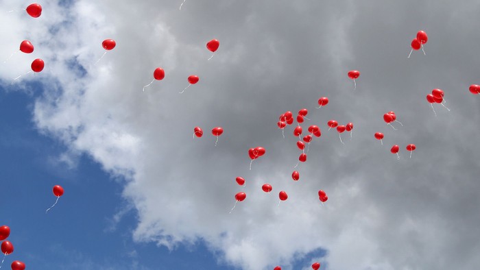 Rote Herzballons steigen in den bewölkten Himmel