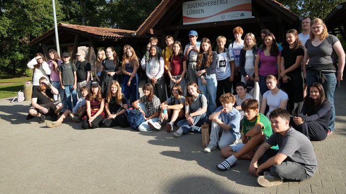 Eine Gruppe von Menschen posiert vor einem kleinen Gebäude mit einem Schild 