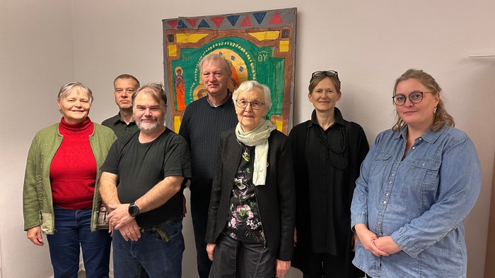 En gruppe af syv personer står sammen foran et farverigt kunstværk.