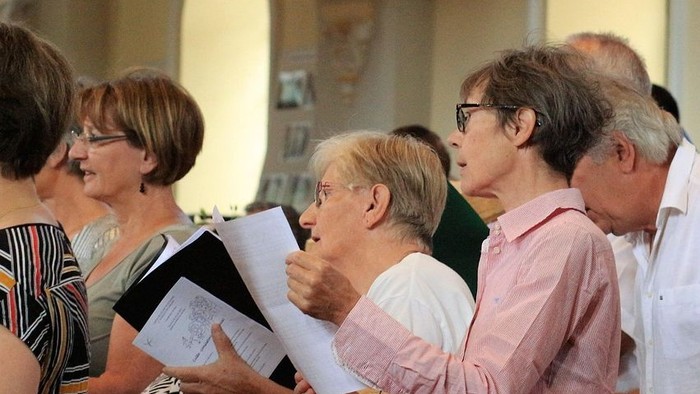 Eine Gruppe von Menschen, die gemeinsam in einer Kirche singen, Notenblätter halten und lächeln.