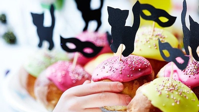 Farverige glaserede donuts med kat-tema dekoration og lys, holdt af en hånd.