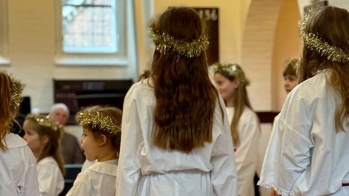 Børn i hvide kjortler med krans af grønt deltager i en ceremoniel procession indendørs.