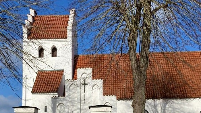 En smuk kirke med røde tag og hvidt murværk, omgivet af træer og en mur.