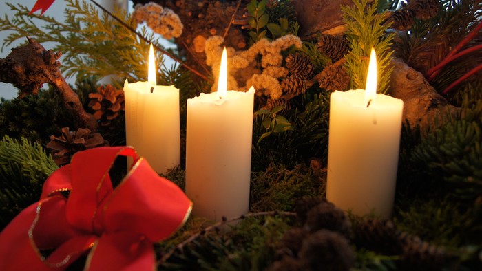 En adventskranse med tre lysende lys og en rød bue.