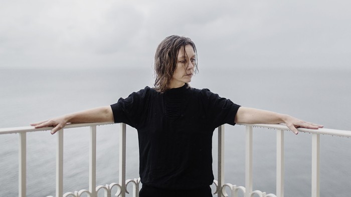 En person i en sort skjorte står på en altan med udsigt over havet.