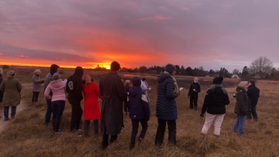 En gruppe af mennesker står i en åben mark og ser solen gå ned.