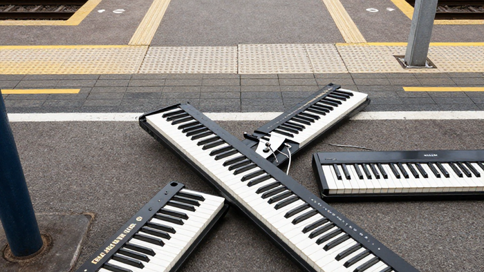 Zwei tragbare Keyboards, die sich auf einem Bahnsteigpflaster kreuzen.