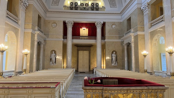 Elegant interiør i en stor kirke med prægtige kirkebænke, søjler og et hævet alterparti.
