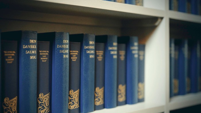 En samling af blå danske Bibler pænt arrangeret på en bibliotekshylde.