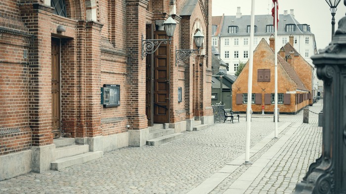 Hyggelig brostensbelagt gade omkranset af historiske murstensbygninger og flagstænger i en europæisk by.
