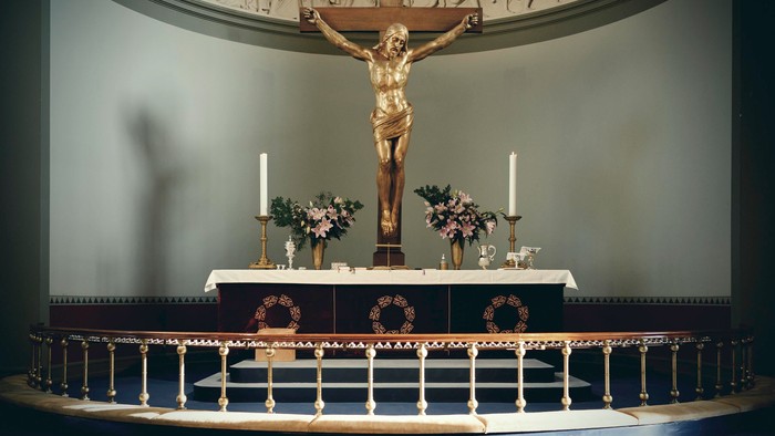 En kirkealter med Jesus Kristus på korset, omgivet af lysestake og blomster.