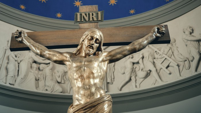 Bronze krucifiks-skulptur af Jesus Kristus med relieffer, der skildrer bibelske begivenheder omkring kuplen.