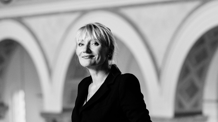 En kvinde står i en arkade med bueformede vinduer bagved.