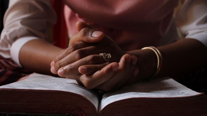 Eine Person hält ein Babyhändchen, während ein aufgeschlagenes Buch darunter liegt.