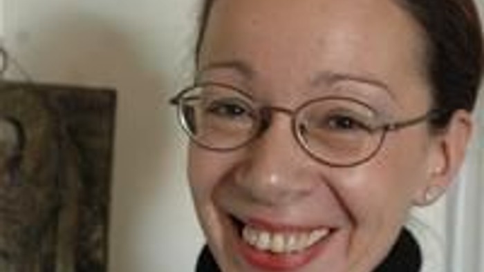 En glad kvinde med briller og rød læbestift, der smiler varmt indenfor.