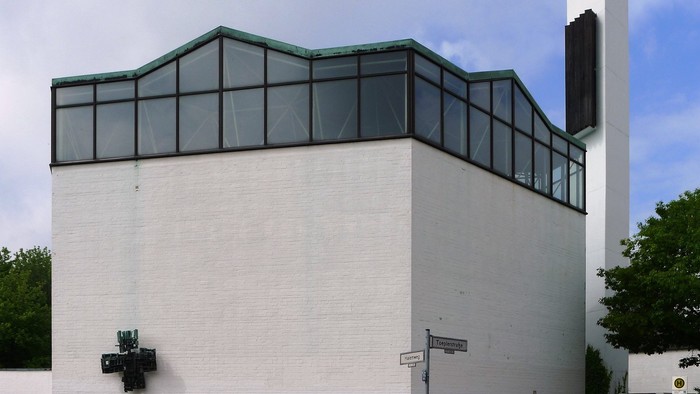 Das Bild zeigt ein modernes weißes Gebäude mit Glasfenstern und einem hohen Kamin.