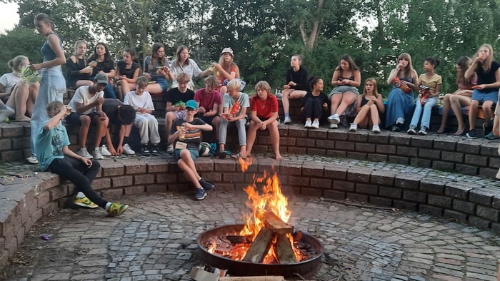 Die Gruppe versammelt sich um ein Lagerfeuer und genießt einen geselligen Abend im Freien mit Freunden.