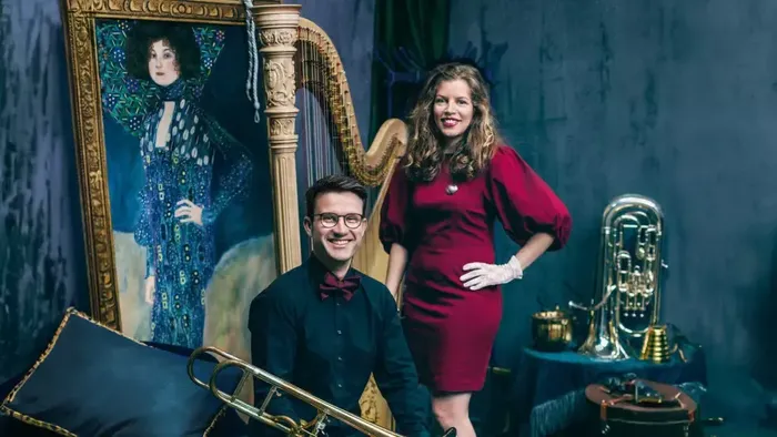 Musiker posieren mit Vintage-Instrumenten und einer verzierten Harfe vor einem künstlerischen Hintergrund.