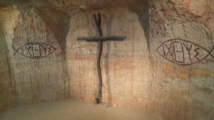 A cross is mounted on a stone wall with fish symbols etched on either side.