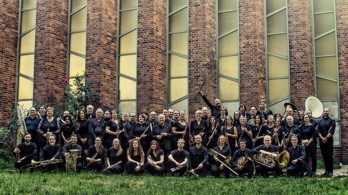 Ein großer Musikverein posiert vor einem modernen Backsteingebäude