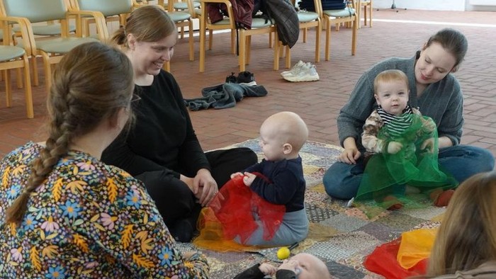En gruppe af voksne og børn spiller på gulvmatte i en lokal.