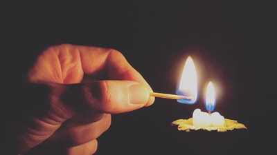 Hånd tænder to lyse pinde over en blomst.