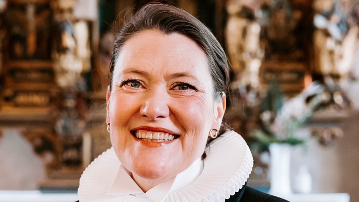 En kvinde i sort jakke med hvid krage står foran en prægtig altertavle.