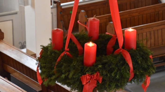 Ein Adventskranz mit vier brennenden Kerzen hängt in einer Kirche