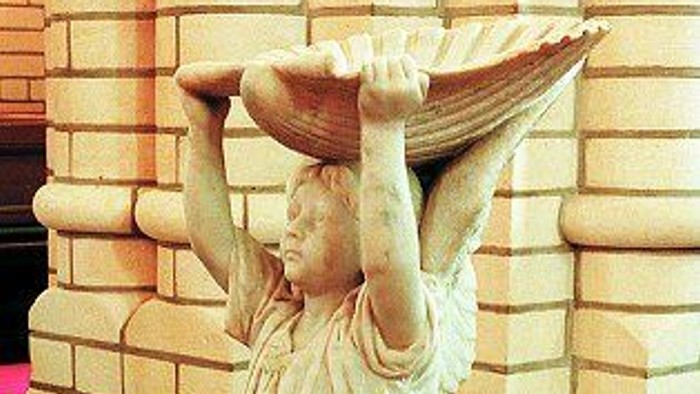 En kvindefigur af marmor med en skål på hodet står på en sokkel.