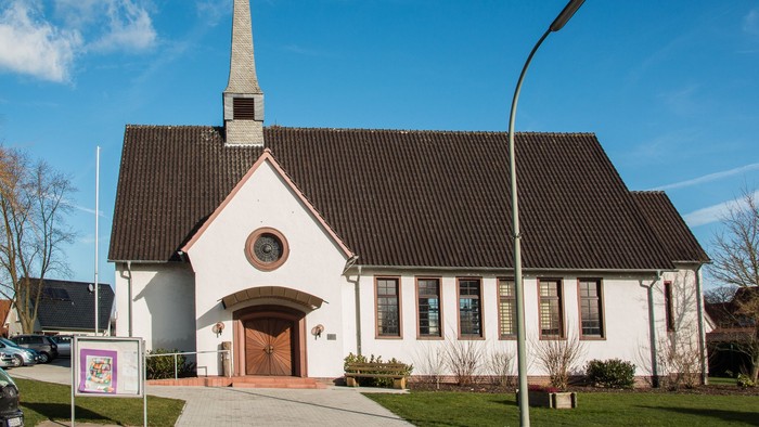 Weiße Kirche mit hohem Turm und schwarzem Dach unter blauem Himmel