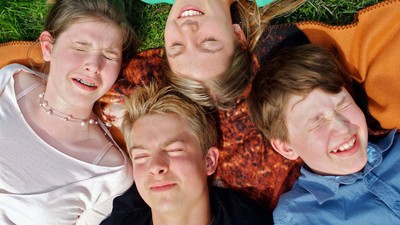 Vier Personen liegen lachend auf einem grünen Rasen.