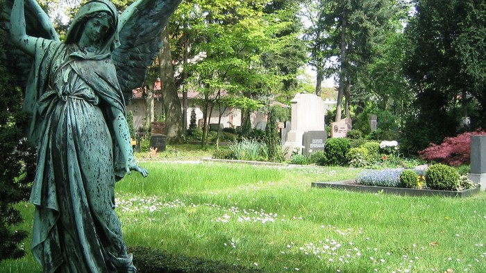 Eine friedvolle Friedhofstatue eines Engels inmitten üppigem Grün und blühenden Blumen.