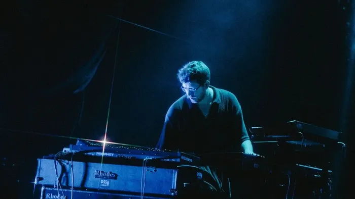 Ein Musiker tritt auf einer Keyboard-Synthesizer-Bühne unter gedämpftem, dramatischem Licht auf.