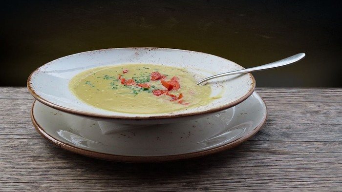 En bolle med grøn suppe og tomater på en hvid tælle under en skovl