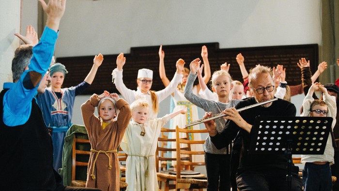 Eine Gruppe führt ein lebhaftes, interaktives Theaterstück mit erhobenen Händen und mittelalterlichen Kostümen in einer Kirche auf.